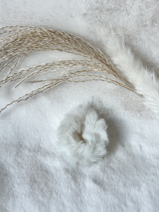 Hellgrauer flauschiger Scrunchie aus weichem Kunstfell, elegant präsentiert auf weißem Stoff mit Pampasgras – luxuriöses Haar-Accessoire von Javi Jewelery