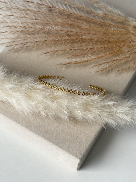 Feiner goldener Armreif mit zarten, miteinander verbundenen Gliedern im filigranen Design, elegant präsentiert auf beigem Stoff mit Pampasgras – Javi Jewelery