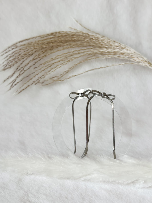 Silberne Ohrringe mit feiner Schleifenform, elegant arrangiert auf hellem Hintergrund mit Pampasgras – zarter, femininer Schmuck von Javi Jewelery