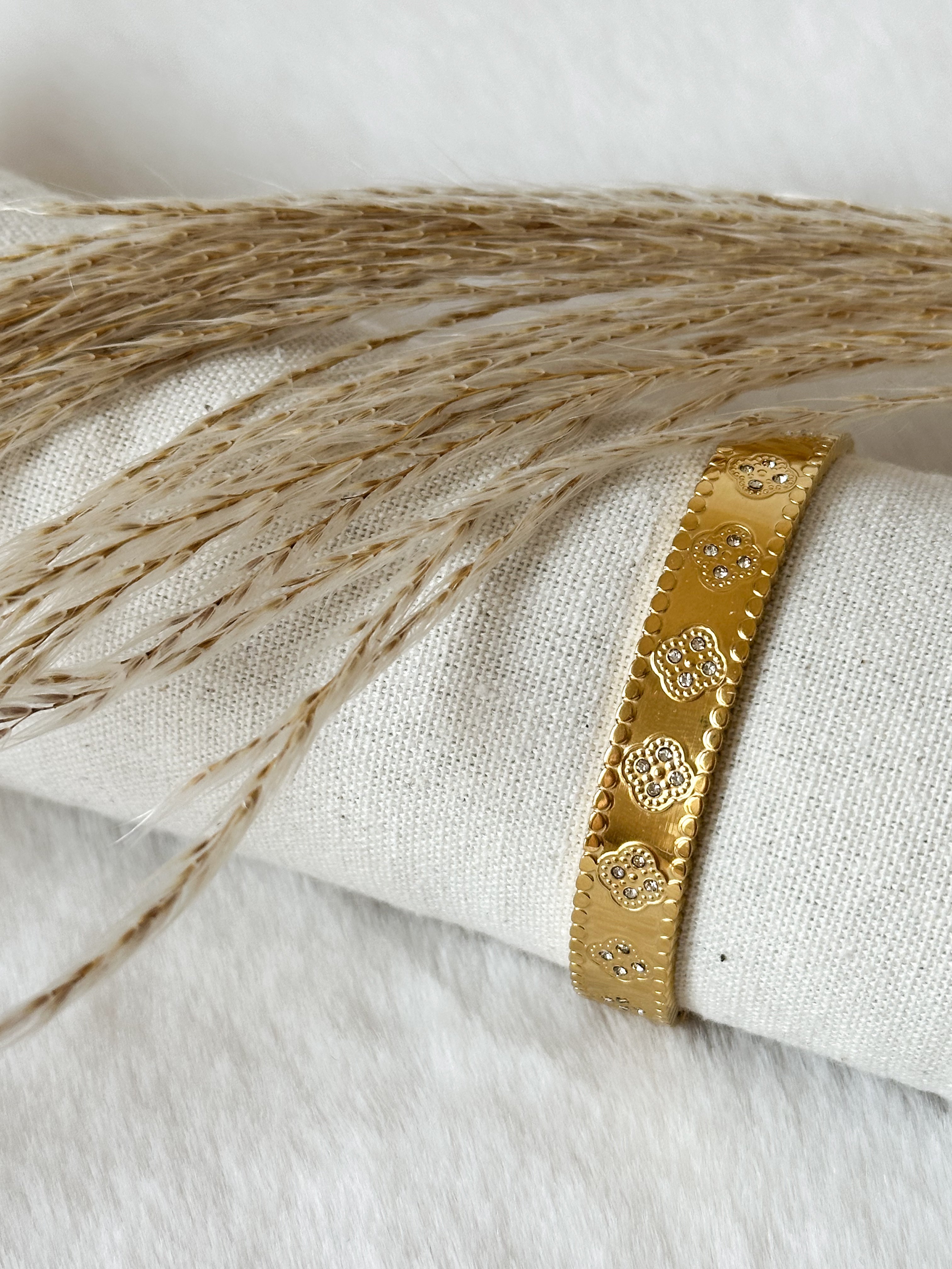 Feiner goldener Armreif mit filigranem Muster im eleganten Boho-Stil, liebevoll präsentiert auf Leinenstoff mit Pampasgras – Javi Jewelery