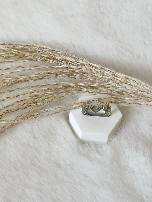 Silberner Ring mit eleganter Muschelform, stilvoll platziert auf weißem Podest mit Pampasgras – moderner Statement-Schmuck von Javi Jewelery